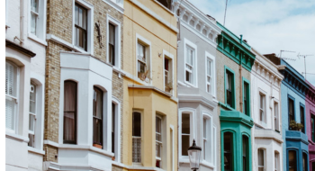 Row of colorful Victorian terraced houses with bay windows on a sunny street.