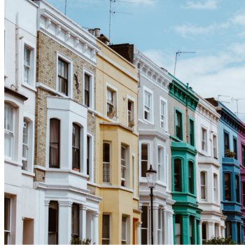 Row of colorful Victorian terraced houses with bay windows on a sunny street.