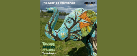 Colorful elephant sculpture painted with trees and flowers, standing on grass near a lake; text reads 'Keeper of Memories' top and 'Trunks Across the Thames' bottom (Thames Hospice).