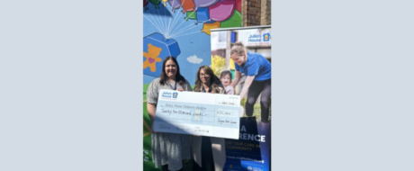 Group of people holding a large donation cheque outdoors in front of a colorful mural, promoting Julia's House children's hospice.