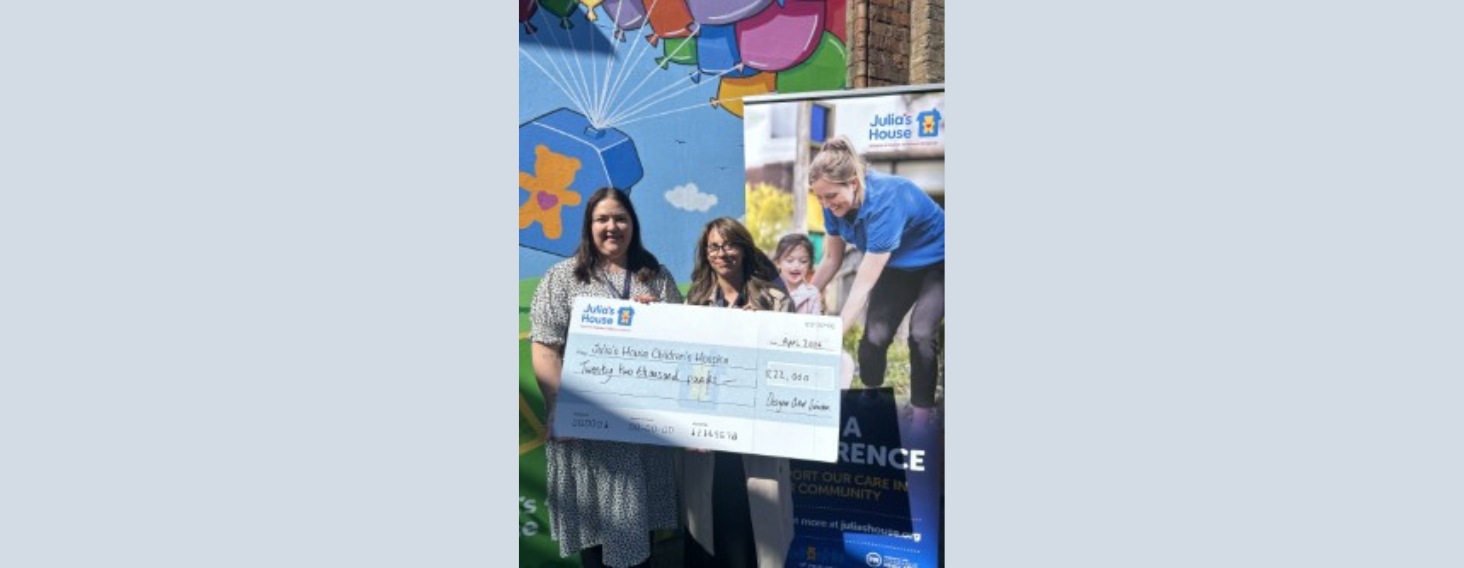 Group of people holding a large donation cheque outdoors in front of a colorful mural, promoting Julia's House children's hospice.