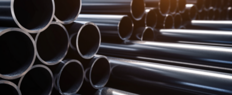 Stacked steel pipes piled in a storage yard, viewed from the side with reflective surfaces outwardly curved ends