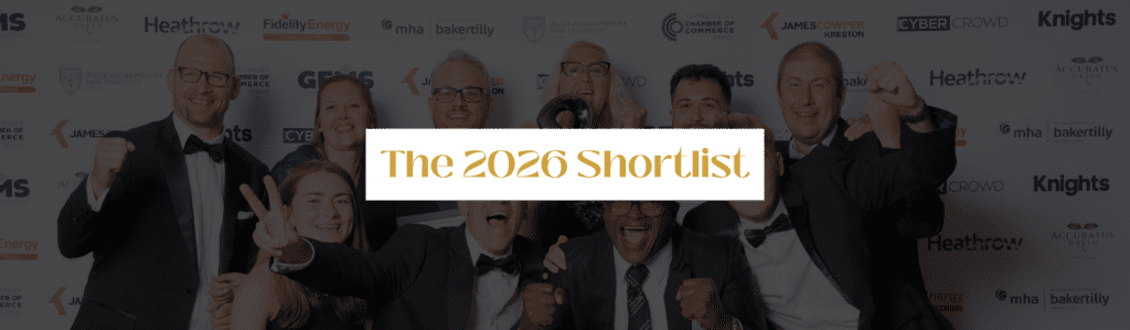 Group of smiling people in tuxedos celebrating at an event; a white banner across the center reads 'The 2026 Shortlist'.
