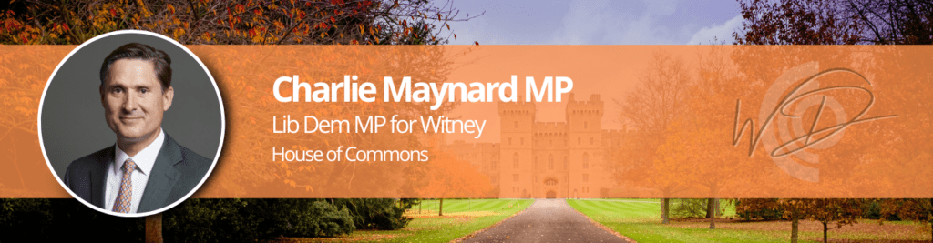 Banner featuring a circular headshot of a man in a suit on the left, with an orange translucent panel containing text about a Lib Dem MP for Witney and the House of Commons, set against autumn trees and a castle backdrop.