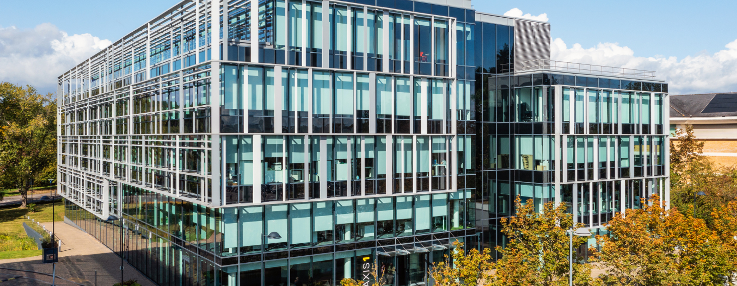 Modern glass office building with vertical and horizontal metal frames under a blue sky, reflecting surroundings in the façade.