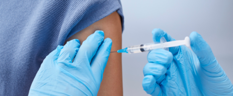Healthcare professional in blue gloves administers a vaccination in a raised arm.