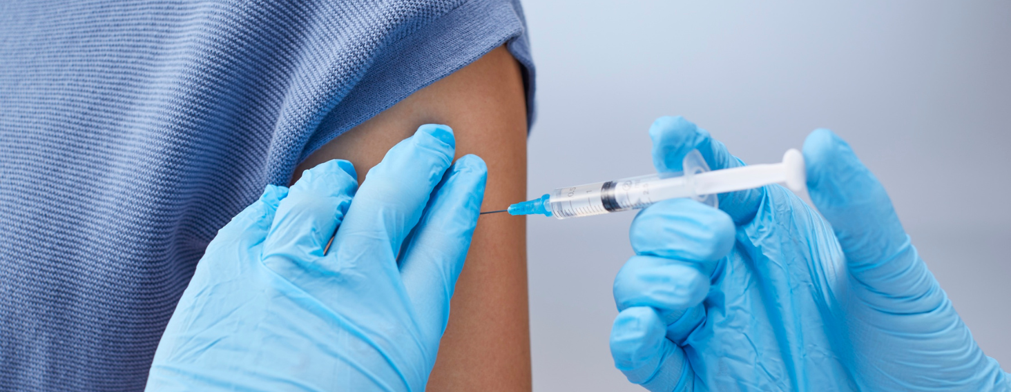 Healthcare professional in blue gloves administers a vaccination in a raised arm.