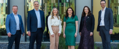 Six professionals stand outside a modern office building, posing for a group photo.