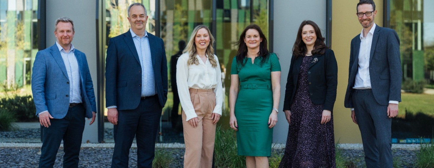 Six professionals stand outside a modern office building, posing for a group photo.