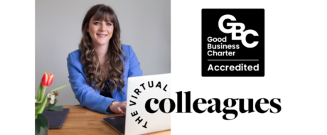 Smiling woman in a blue blazer sits at a desk with a laptop, branding shows 'Virtual Colleagues' and a Good Business Charter Accredited logo nearby.