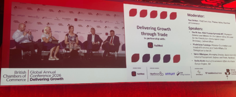 Panel of five speakers seated on a stage during a conference; left screen shows 'British Chambers of Commerce Global Annual Conference 2026: Delivering Growth' and partner logos, right screen lists moderator and speakers.