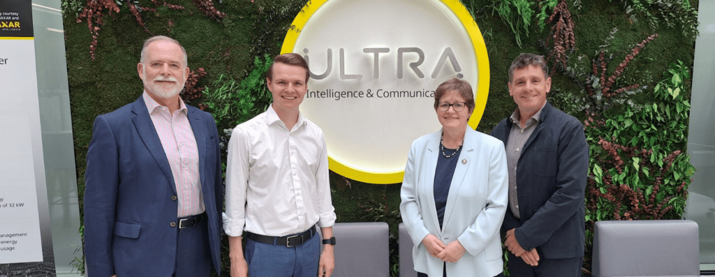 Four professionals stand side by side in front of a circular ULTRA sign on a green living wall, posing for a group photo in a corporate setting.