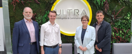 Four professionals stand side by side in front of a circular ULTRA sign on a green living wall, posing for a group photo in a corporate setting.