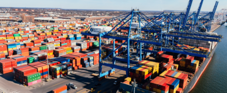 Large container port with colorful stacked shipping containers and tall blue gantry cranes over a docked cargo ship area