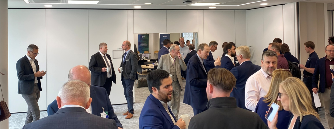 Group of professionals in business attire mingle and chat at a modern office reception with coffee cups and networking in the background.