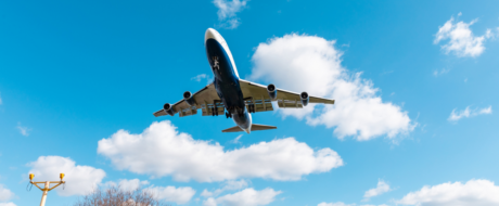 Low-angle view of a large commercial airliner flying overhead against a blue sky with clouds; airport light pole visible bottom left.