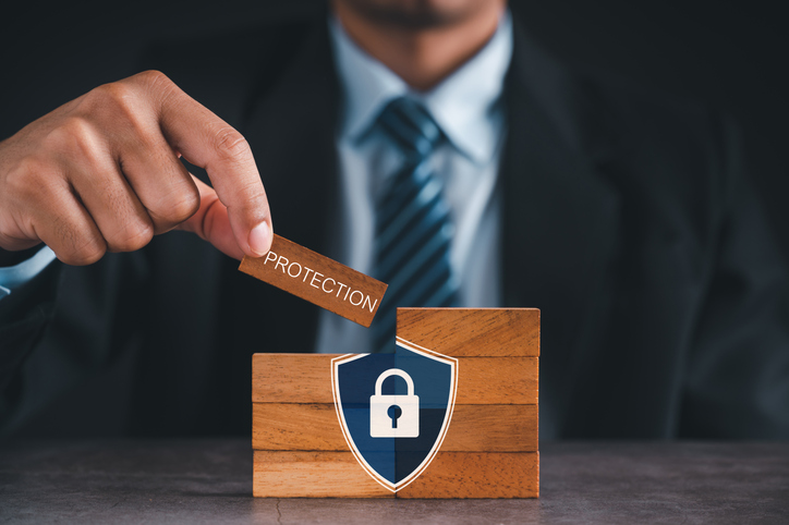 Hand places a wooden tile labeled 'Protection' onto a block with a shield and padlock, symbolizing security.