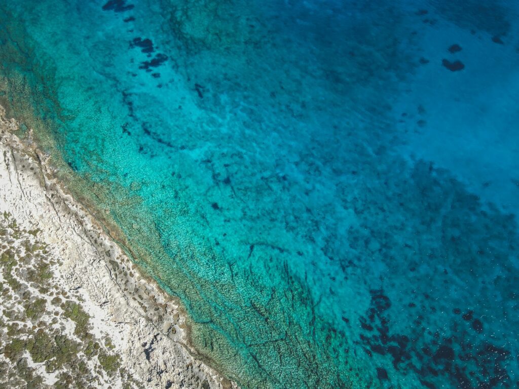 Aerial view of turquoise water along a rocky coastline, with clear shallow areas near shore.