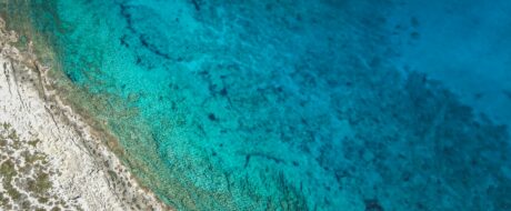 Aerial view of turquoise water along a rocky coastline, with clear shallow areas near shore.