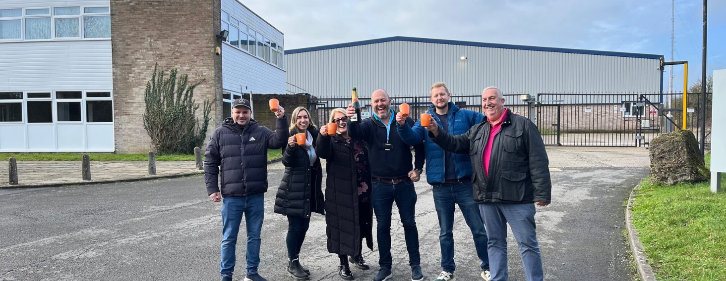 NEW - News item size 61 | Thames Valley Chamber of Commerce Eight people stand outside an industrial building, toasting with orange cups to celebrate together.