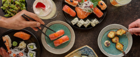 Top-down view of a shared sushi feast with salmon nigiri, rolls, edamame, and skewered bites on a dark table.