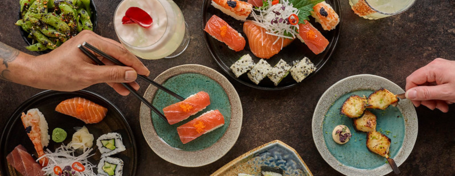 NEW - News item size 62 | Thames Valley Chamber of Commerce Top-down view of a shared sushi feast with salmon nigiri, rolls, edamame, and skewered bites on a dark table.