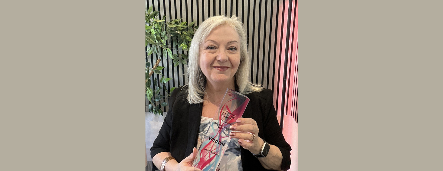 NEW - News item size 65 | Thames Valley Chamber of Commerce Smiling woman in a black blazer holding a glass award labeled WINNER, standing beside a striped wall and plants.