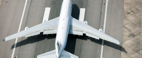Top-down view of a large white commercial airplane aligned on a gray runway, wings spread wide and shadowed on the tarmac