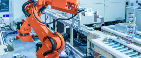 Orange robotic arm functioning on a manufacturing line with conveyors and machinery in a high-tech factory setting.