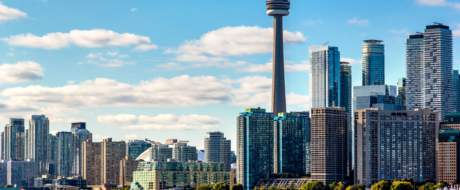 Toronto skyline with the CN Tower towering above glass skyscrapers on a sunny day.