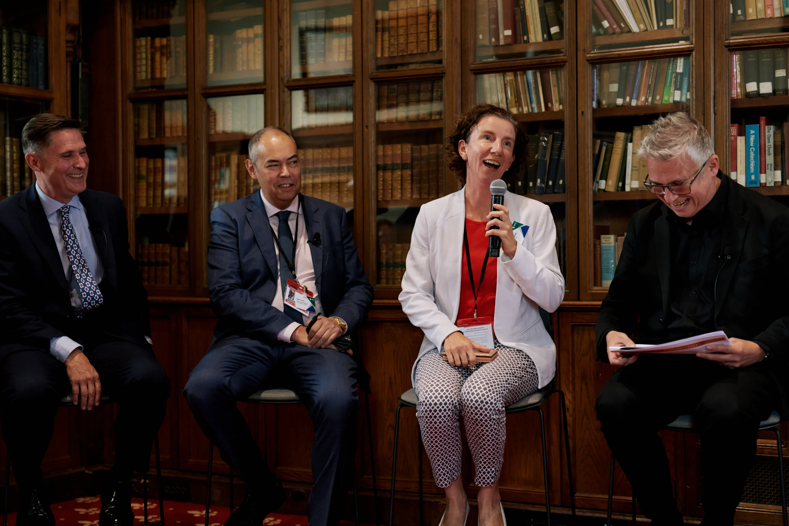Panel of four people in a library, the woman center-right speaks into a microphone and others listen smilingly.
