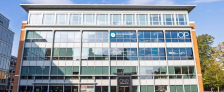 Modern glass-front office building with brick columns on the sides; blue Boyes Turner sign on the second floor and large reflecting windows across the façade.