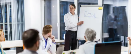 Man presenting a graph on a flip chart to colleagues in a modern conference room.