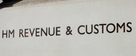 Sign reading 'HM Revenue & Customs' on a white concrete wall outside a building, showing the department name clearly