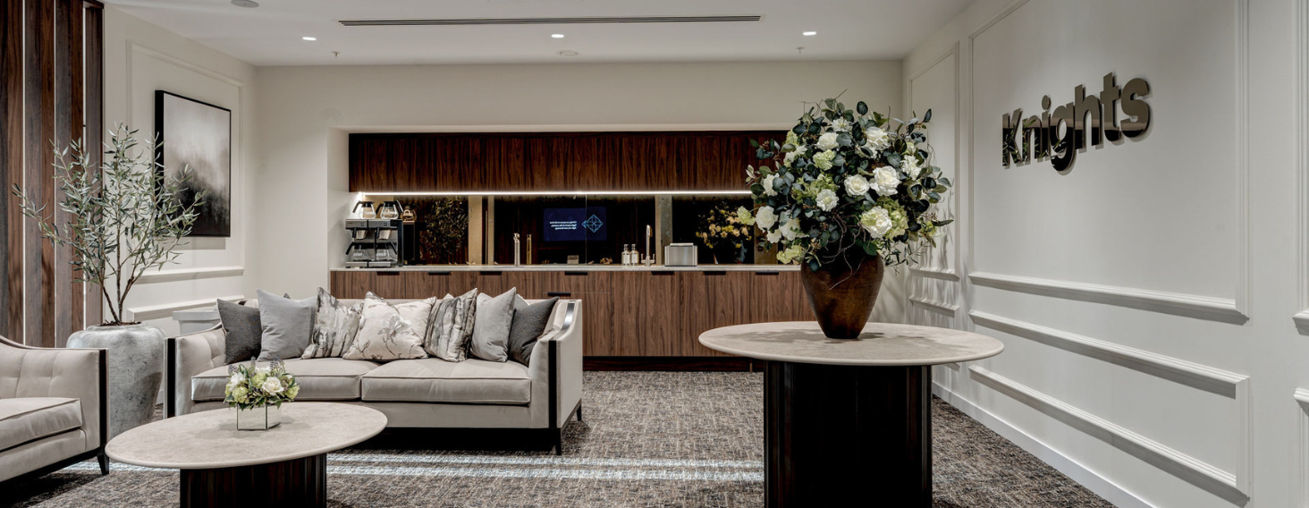 NEW - News item size 95 | Thames Valley Chamber of Commerce Elegant hotel lobby with beige sectional sofa, round marble tables, and a large vase of white flowers; reception bar in the back and 'Knights' sign on the wall.