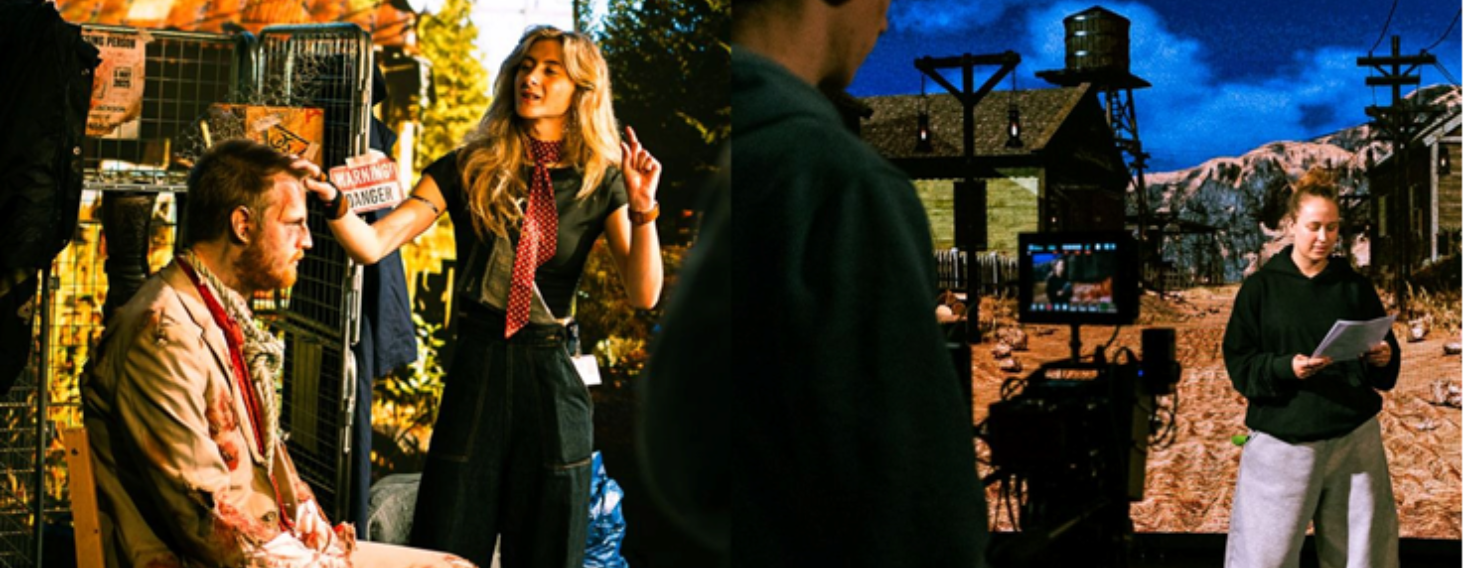 Behind-the-scenes of a film shoot: an actor sits in makeup while a crew member explains something nearby, with equipment around them.",